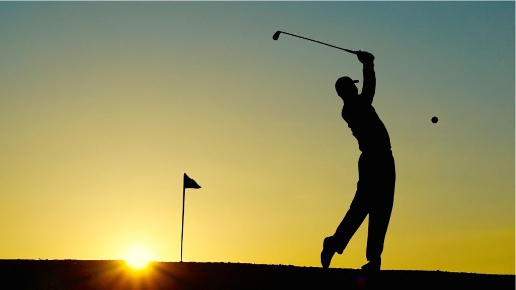 Photograph of silhouetted golfer hitting the ball as the sunsets